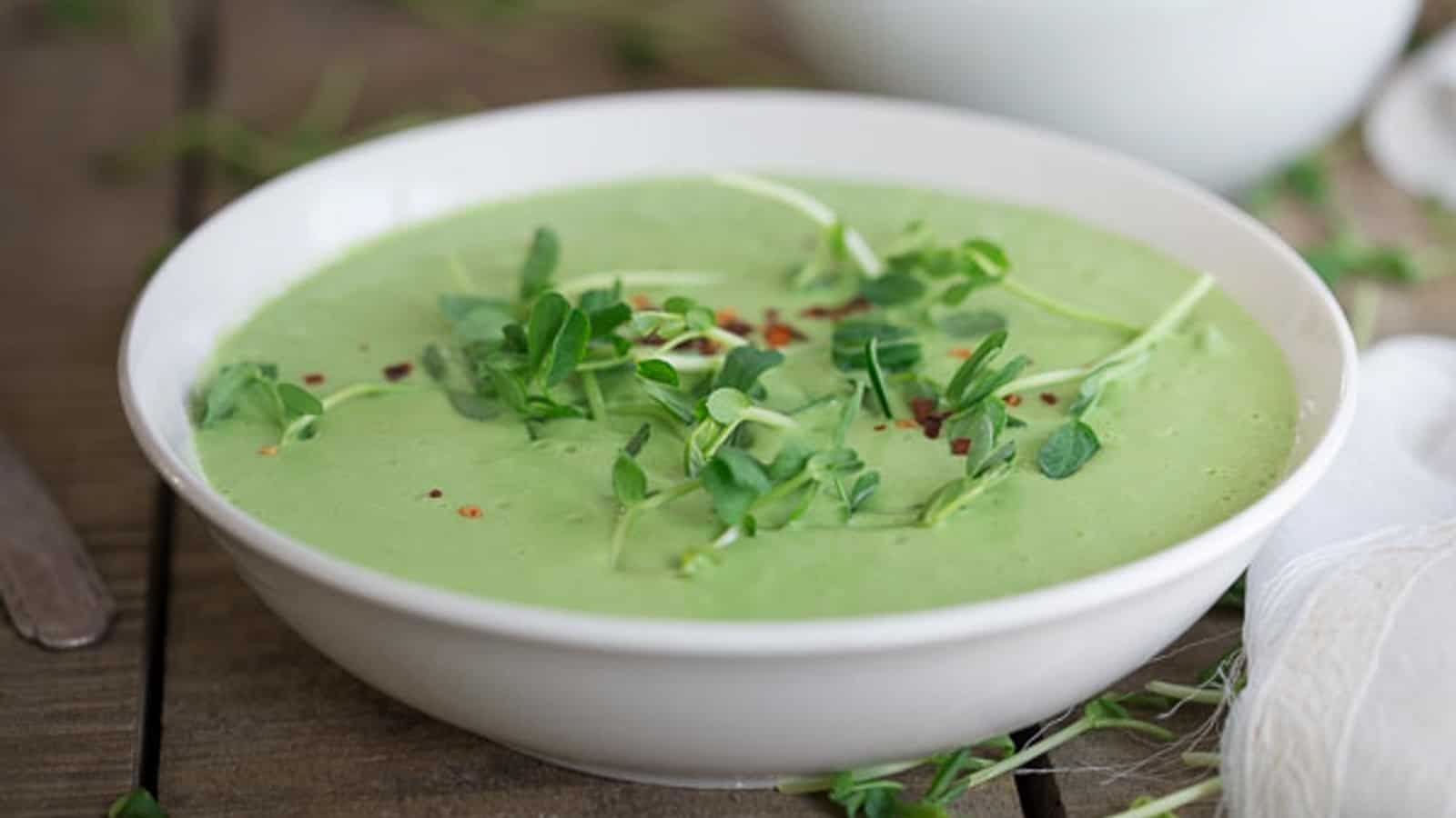 Thai pea soup garnished with pea shoots in a white bowl.