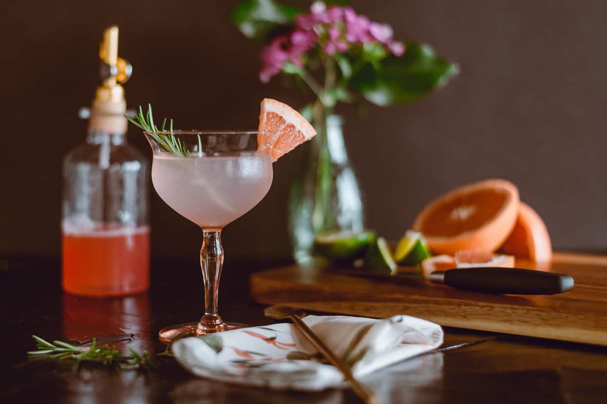A grapefruit cocktail next to a bottle of pink simple syrup.