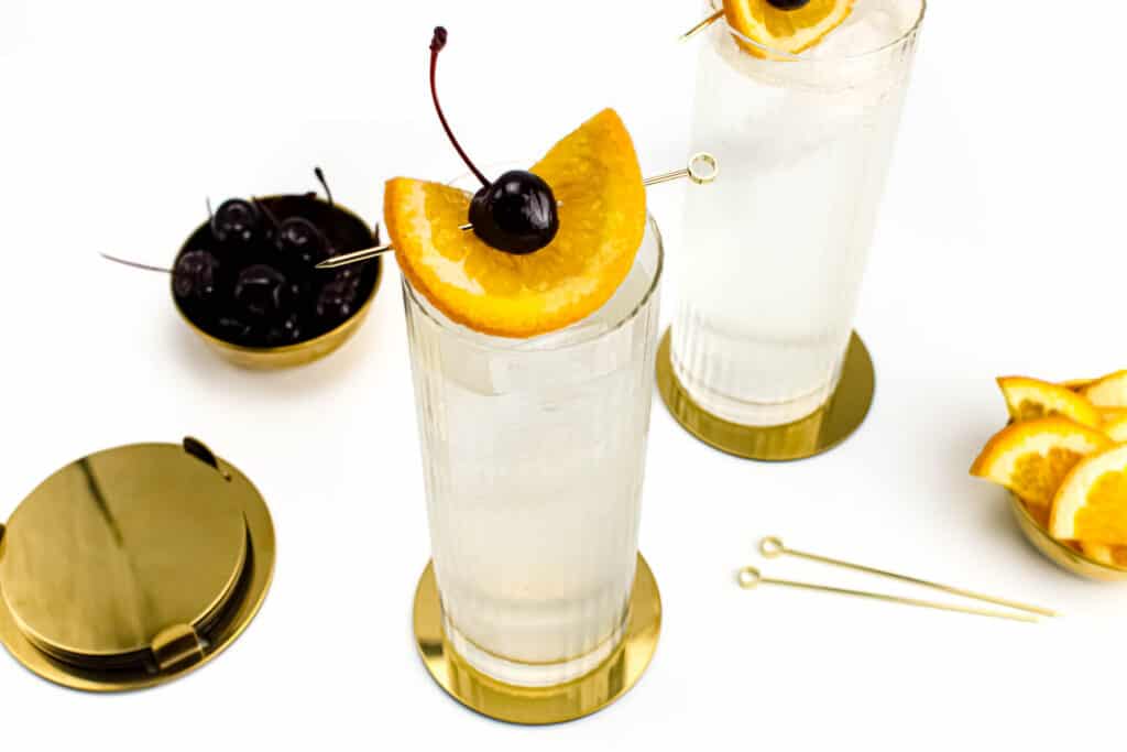 Two Tom Collins Sodas alongside fruit garnishes.