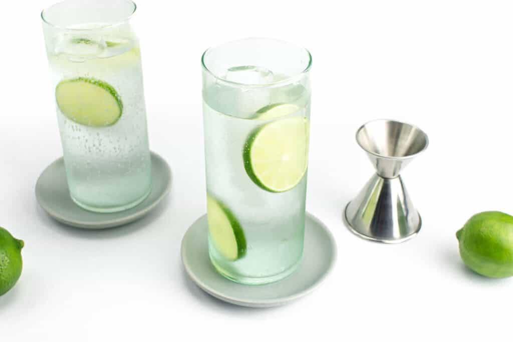 a vodka soda next to a silver jigger and limes.