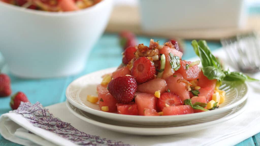 Watermelon bacon salad garnished with basil leaves on a white plate.