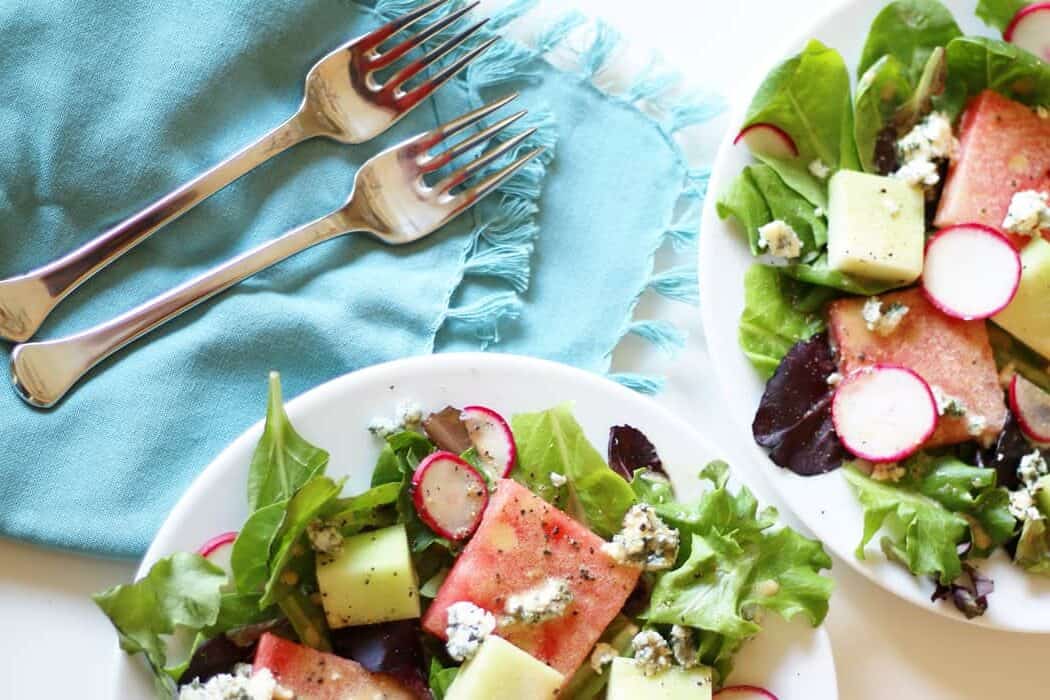 two green salads with watermelon with forks on blue napkins.