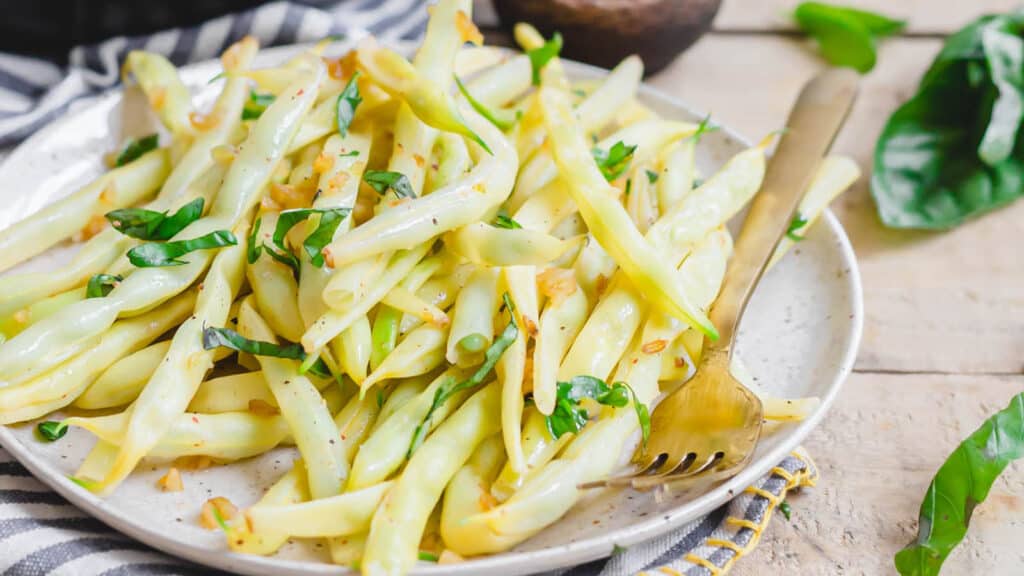 Wax beans with garlic and basil on a plate with a fork.