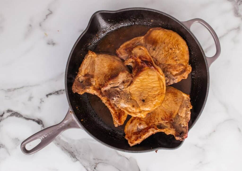 Pork chops piled in skillet.