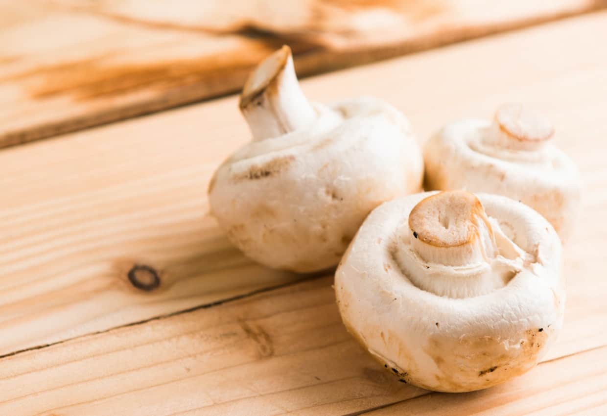 White button mushrooms on a wooden surface.