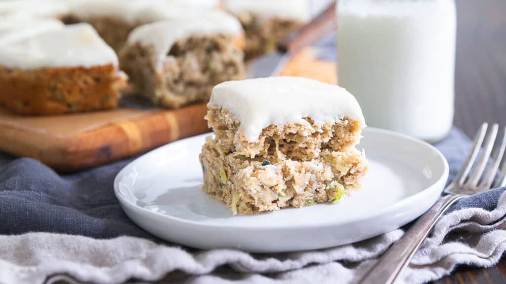 Zucchini bars with cream cheese frosting on a white plate.