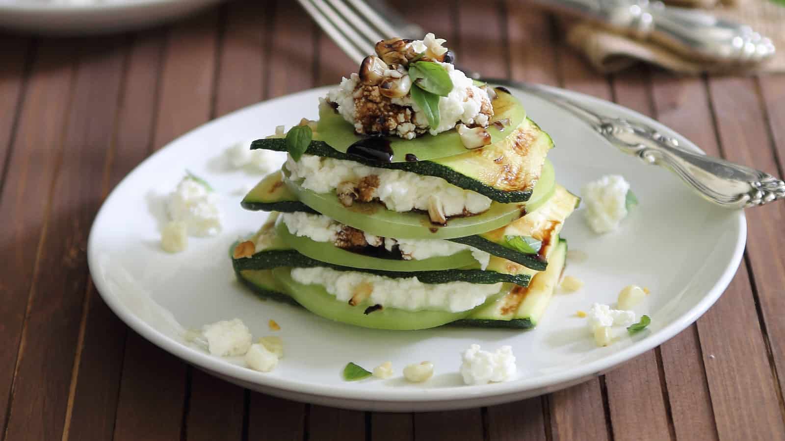 Grilled zucchini stacks with ricotta and green tomatoes on a plate.