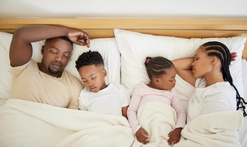 An African-American family of four napping together in bed.