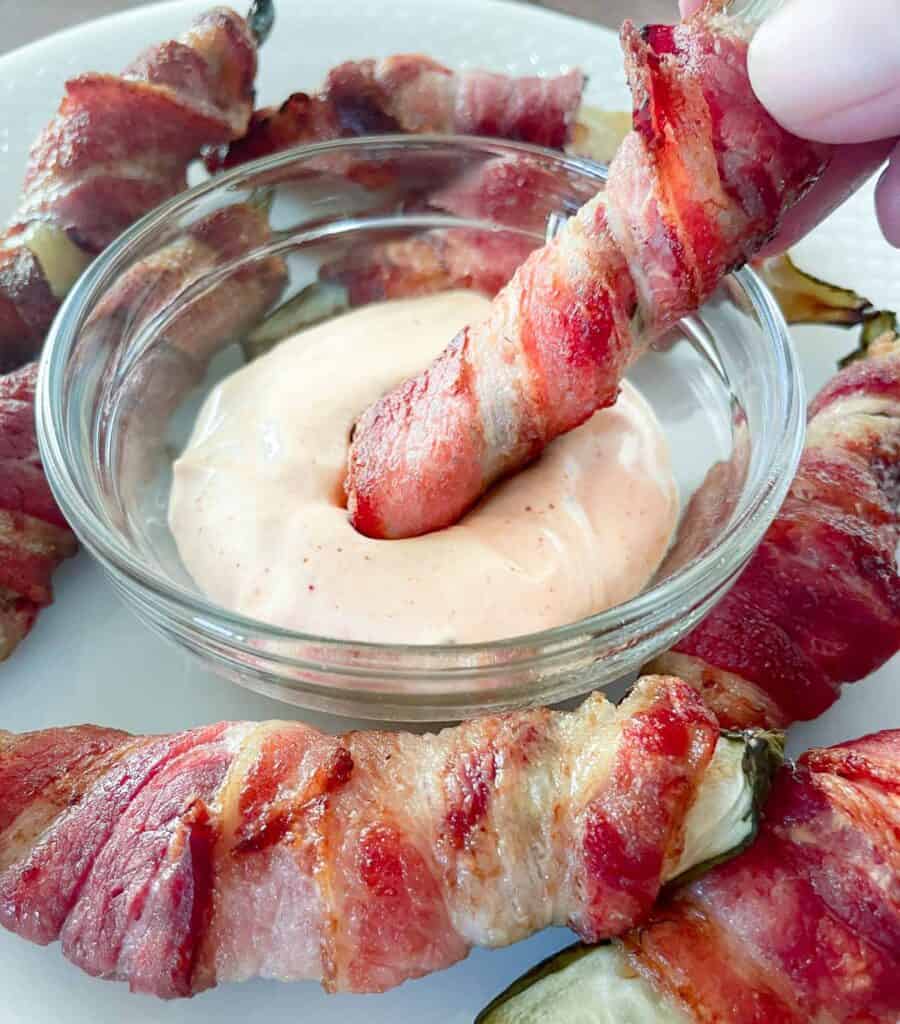 Bacon wrapped pickle being dipped in spicy sriracha mayo. 