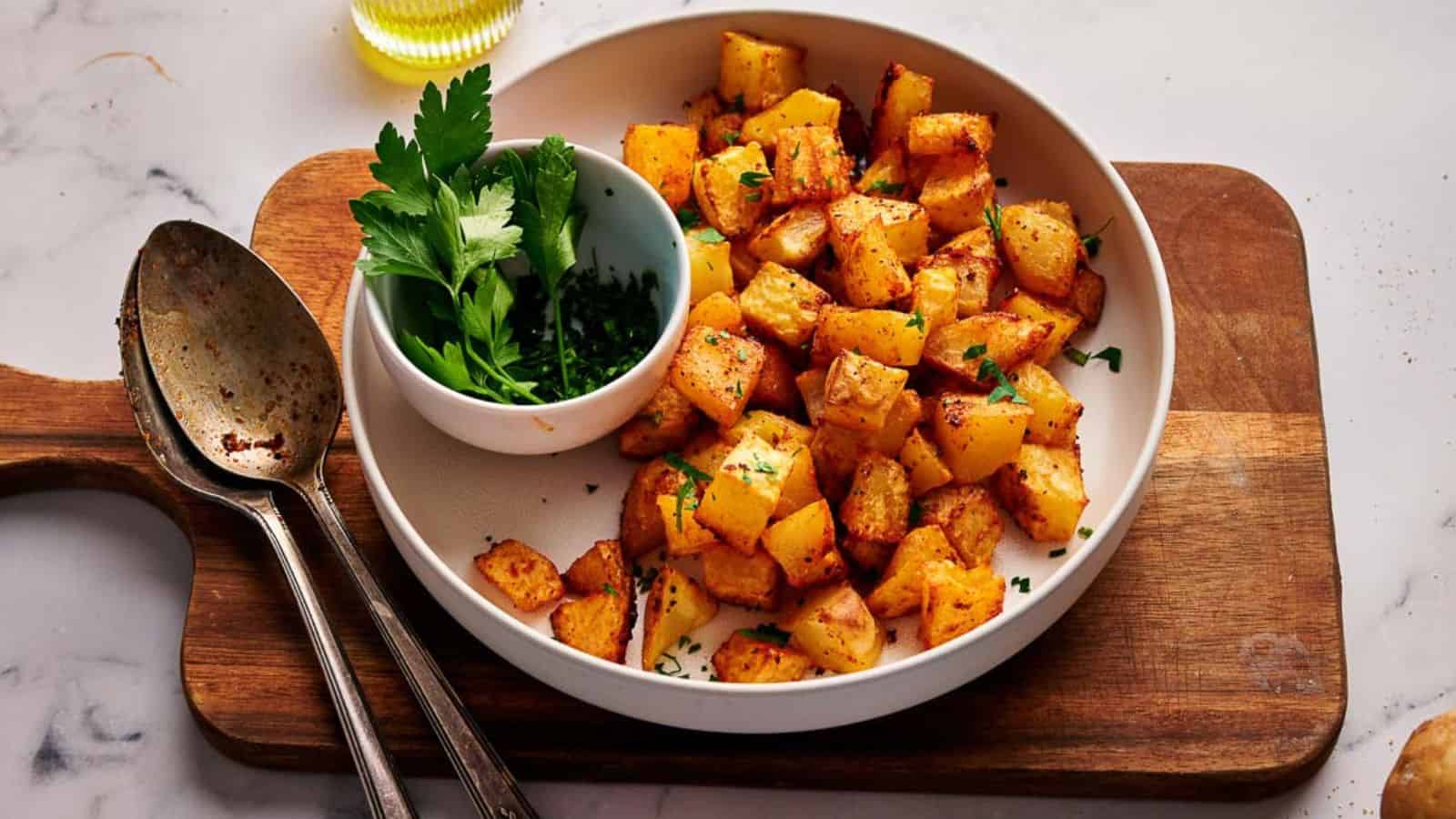 Breakfast potatoes in a serving bowl, with serving spoons and a small bowl of fresh parsley.