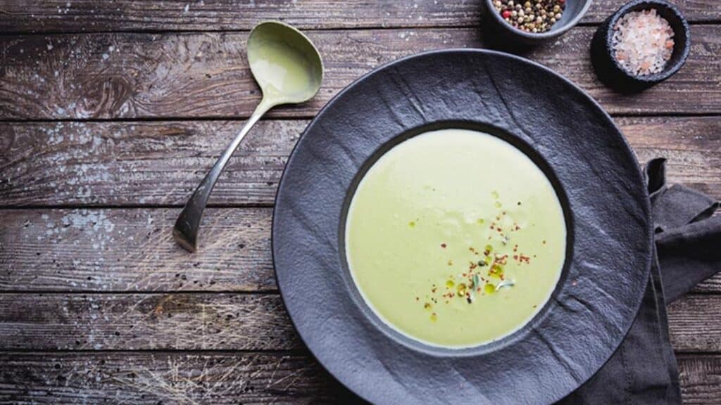 Avocado Bone Broth in black bowl with ladle on wooden background.