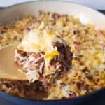 Image shows a closeup of a spoon holding some Cheesy Beef and Rice Casserole with the full skillet behind it.