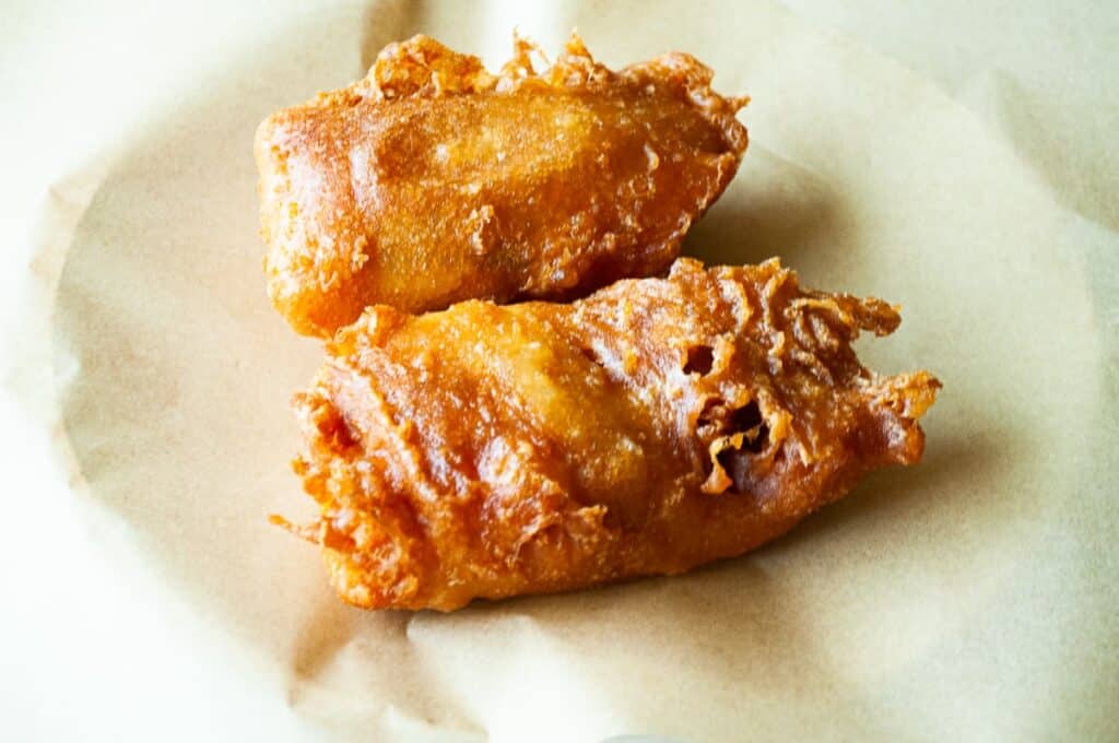 Two pieces of beer battered salmon on a piece of parchment paper. 