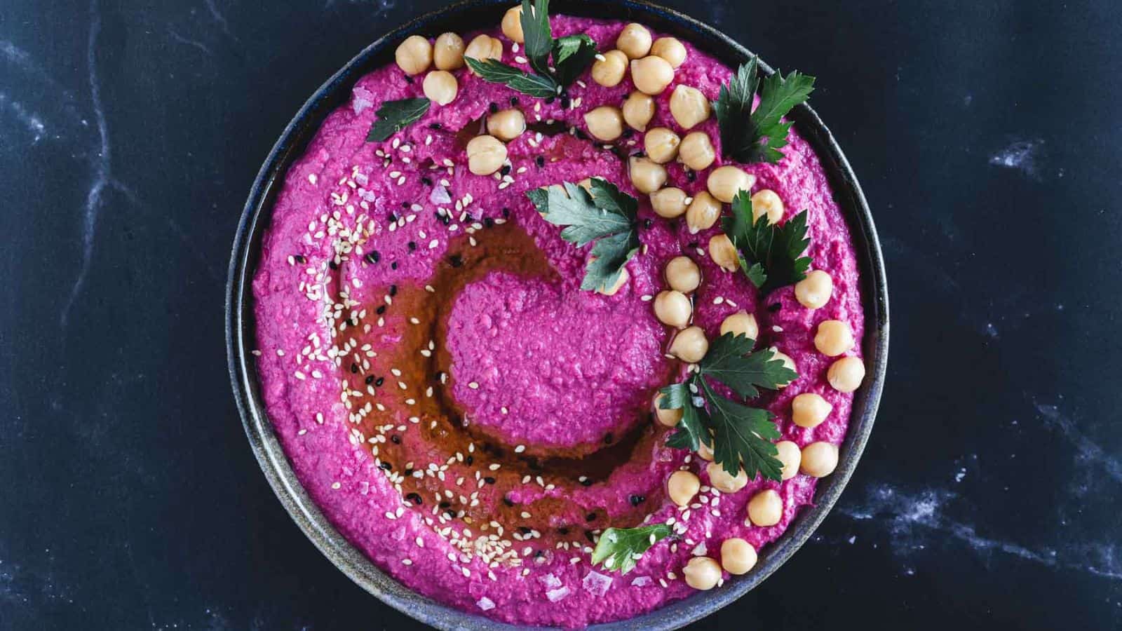 Overhead view of beet hummus with chickpeas and sesame seeds.