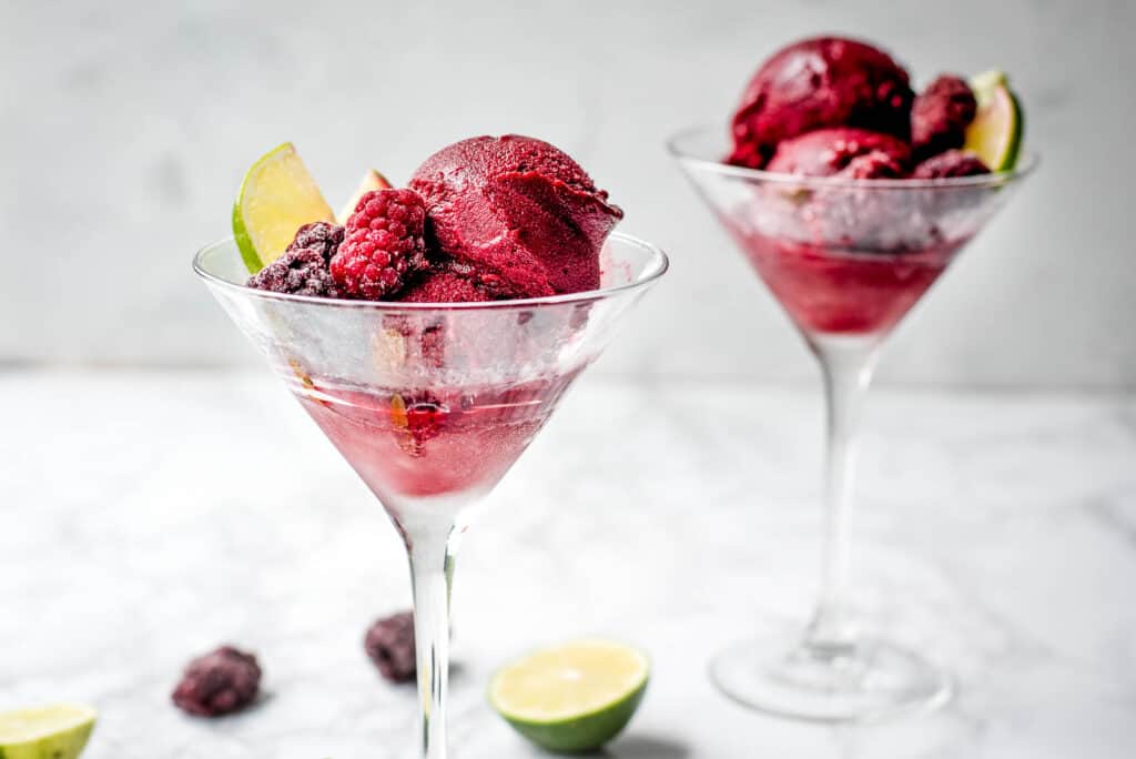 Two servings of blackberry lime sorbet in stemmed martini glasses, garnished with frozen berries.