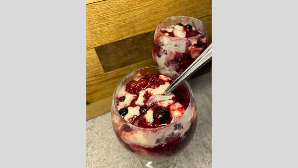 Blueberry melba parfaits in wine glasses with wooden background.