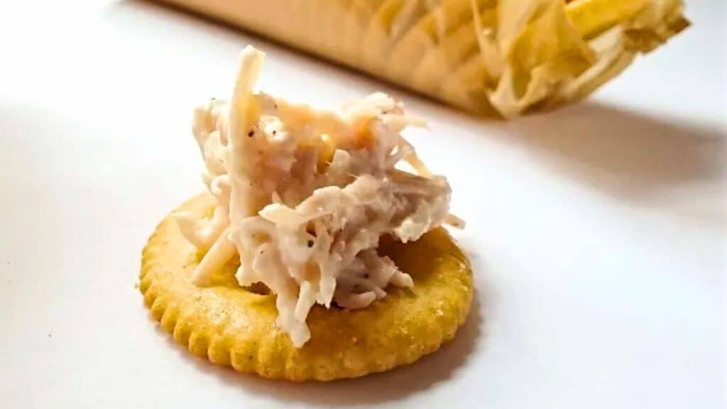 Image shows Canned Chicken Salad on a single Ritz cracker with a sleeve of Ritz crackers in the background.