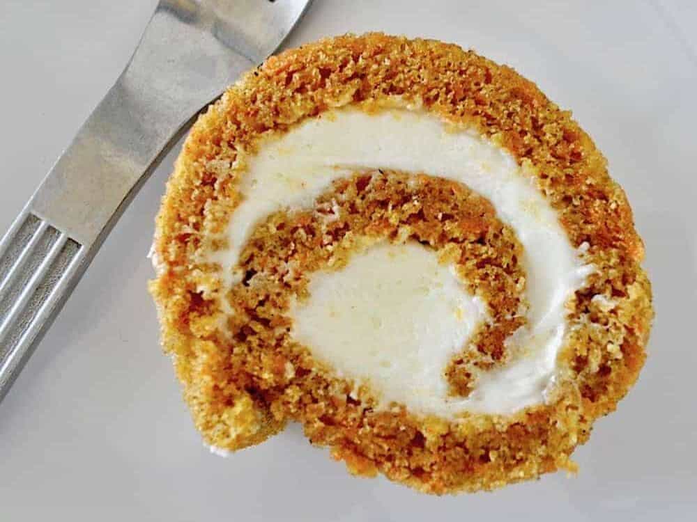Slice of carrot cake roll on a plate with a fork.