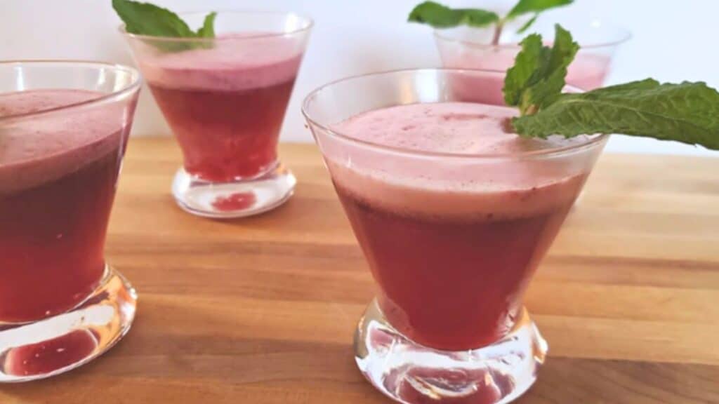 Image shows four cocktail glasses with Cherry Fizz Cocktail in them and a mint sprig on top.