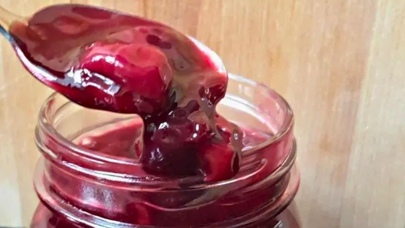 Image shows a close up of a jar of Cherry Syrup with a spoon holding some just above it.