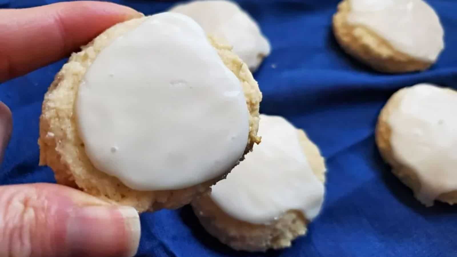Image shows a fingers holding a Chewy Lemon Cookie with more in the background.