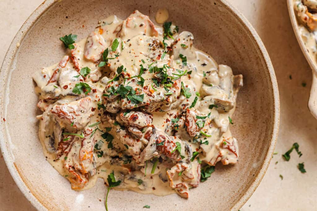 A dish of chicken with creamy mushroom sauce garnished with fresh herbs.