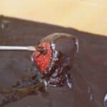 Image shows a fondue fork dipping a strawberry into chocolate fondue.