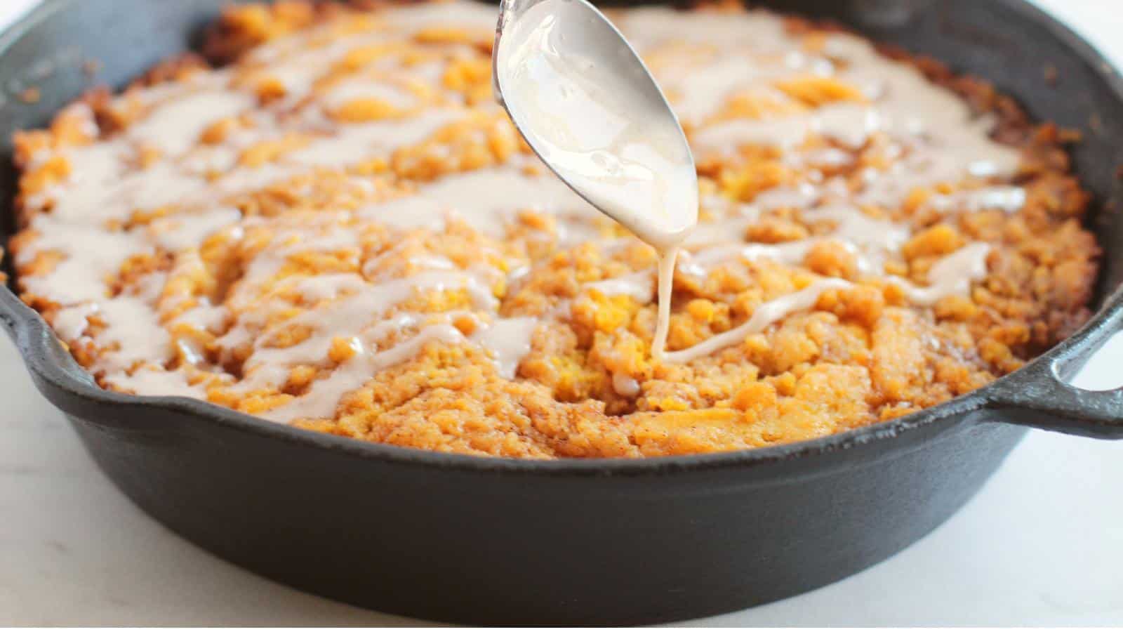 Cinnamon roll pumpkin skillet cake with icing drizzled from spoon.