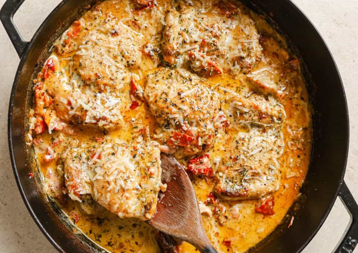 A skillet of creamy sun dried tomato chicken with a wooden spoon.