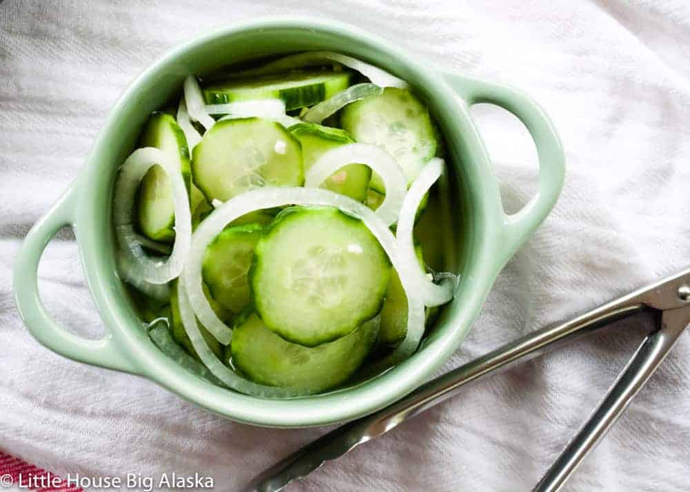 Cucumbers an onions in a small round green dish with tongs to the side of the bowl.