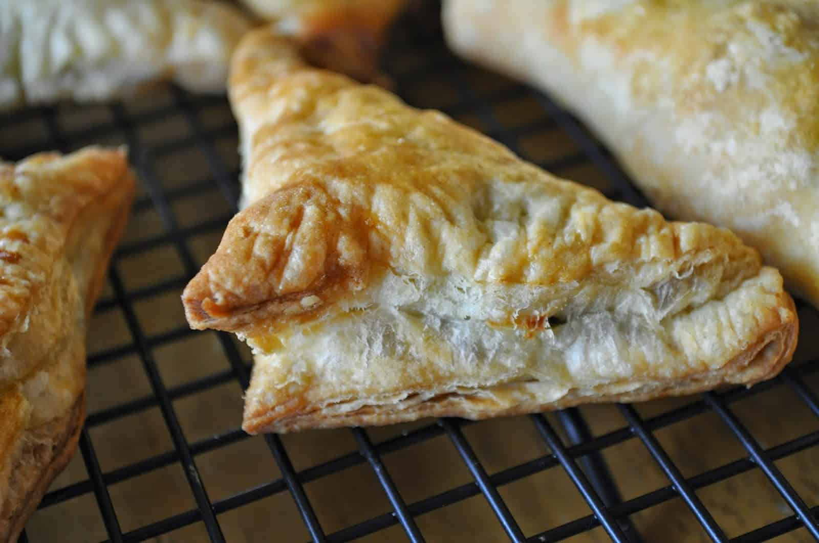 Puff pastry spanakopita triangles on a wire cooling rack. 