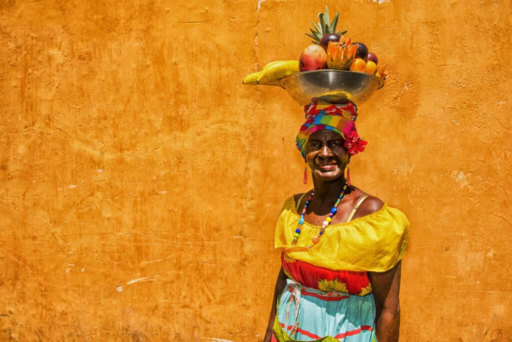 Colombian woman wearing traditional clothes with fruit basket on head.