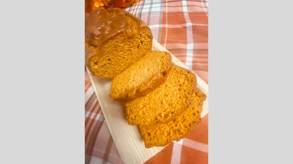 Loaf of pumpkin bread on wooden board with three slices cut off.