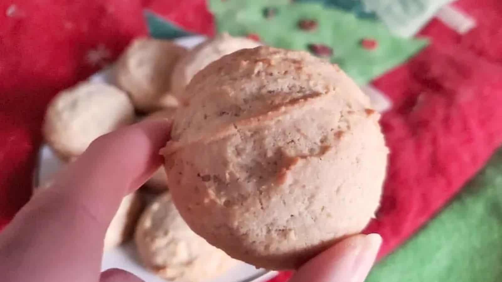 Image shows a hand holding an Egg Nog Cookie over a plate of more cookies.