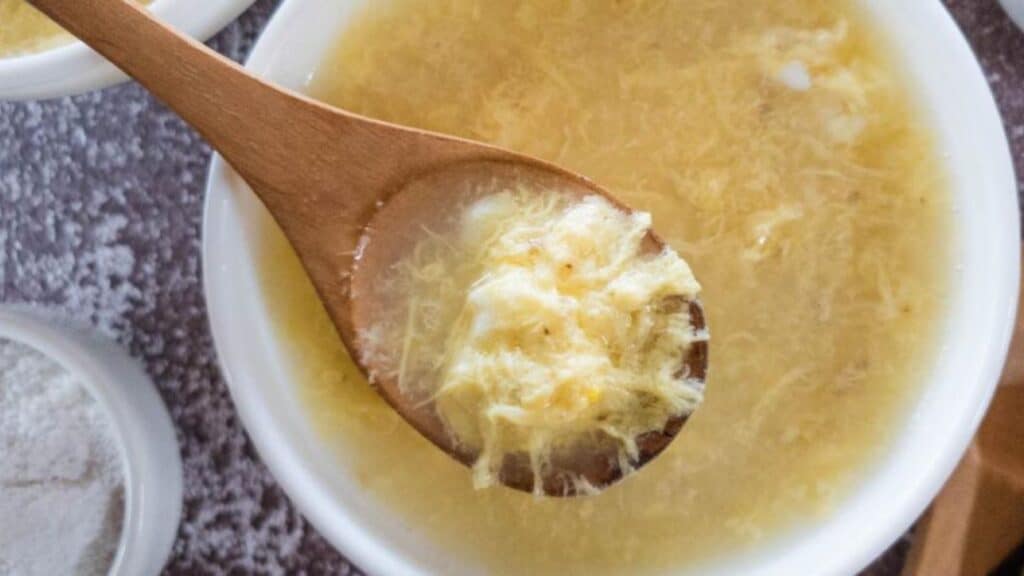 Plain Egg Drop Soup in white bowl with wooden spoon.