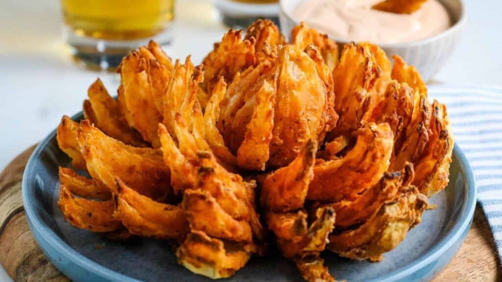 Blooming onion on a plate with sauce in the background.