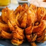 Blooming onion on a plate with sauce in the background.