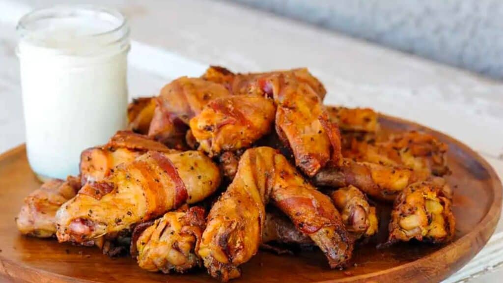 Platter of bacon wrapped chicken wings with side of blue cheese.