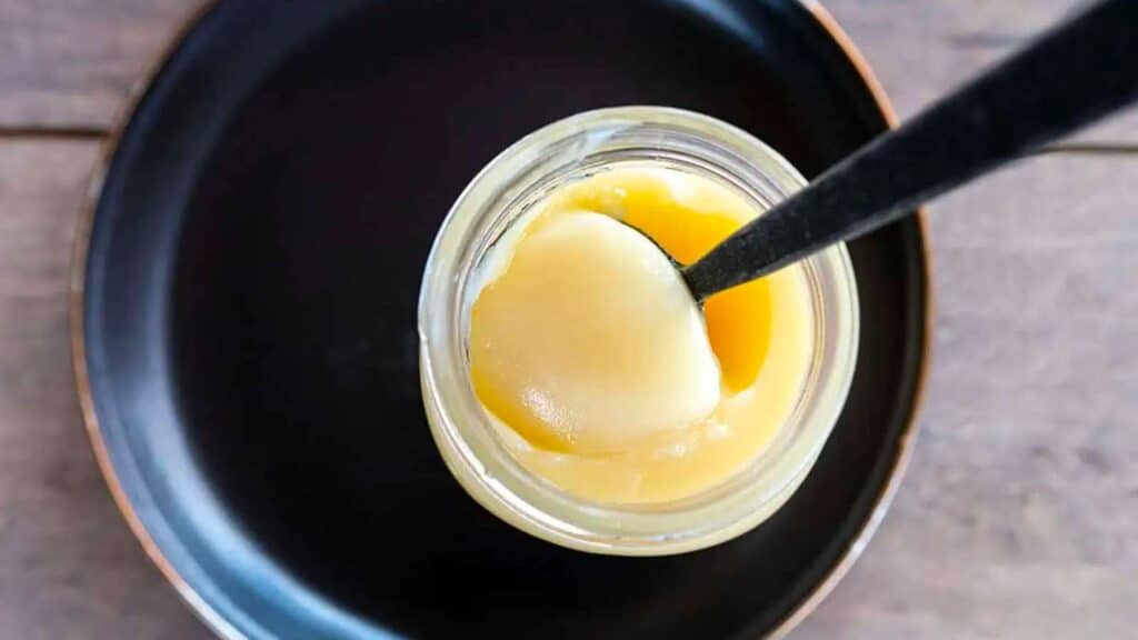 Spooning out a scoop of beef tallow from a jar.