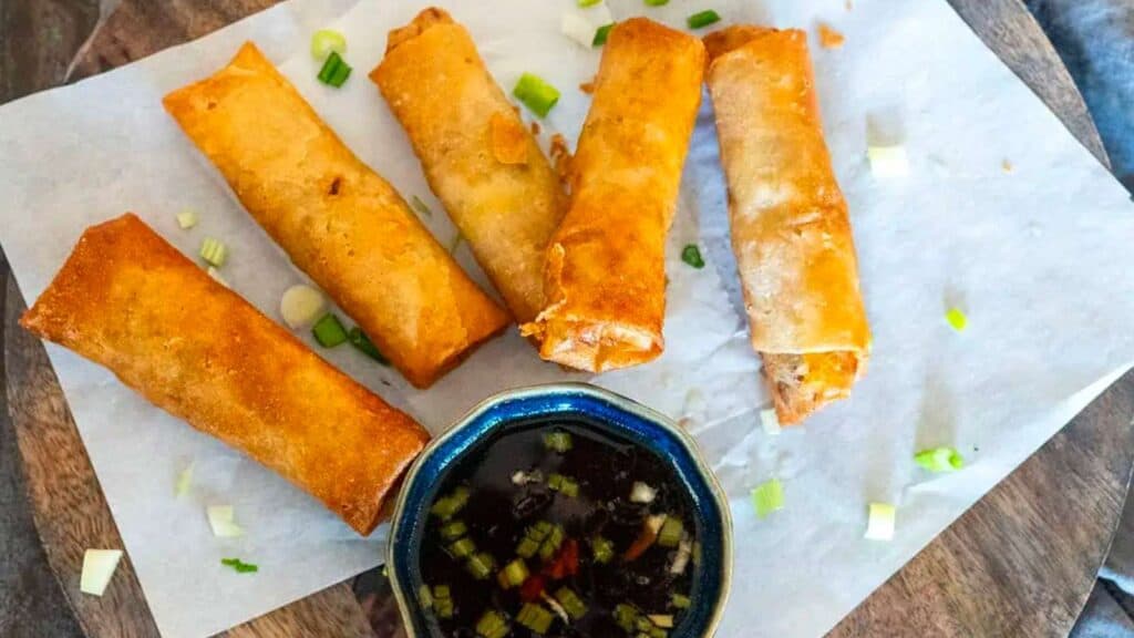 five chicken lumpia on a platter with a bowl of soy vinegar dipping sauce.