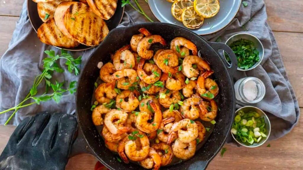 Skillet of Memphis BBQ shrimp with grilled bread and lemons.