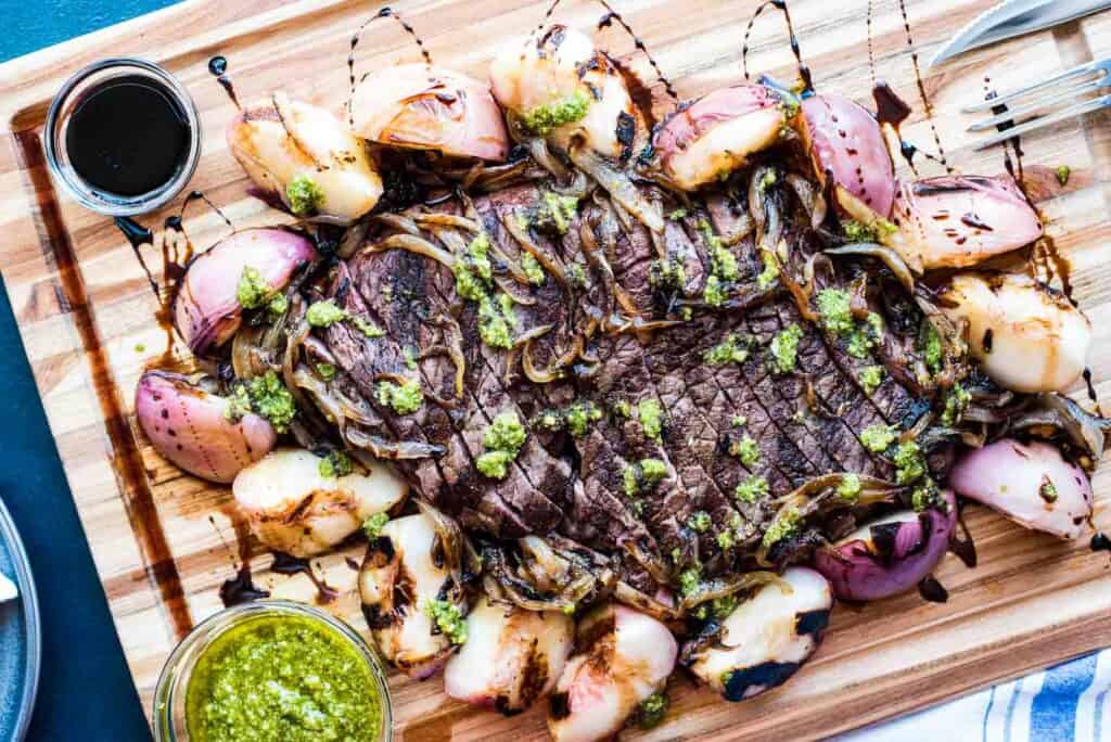 Grilled steak with peaches and onions on a wooden cutting board.