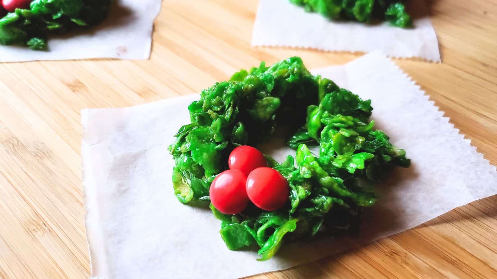 Image shows Holly Wreath Cookies on small pieces of parchment paper sitting on a wooden table.