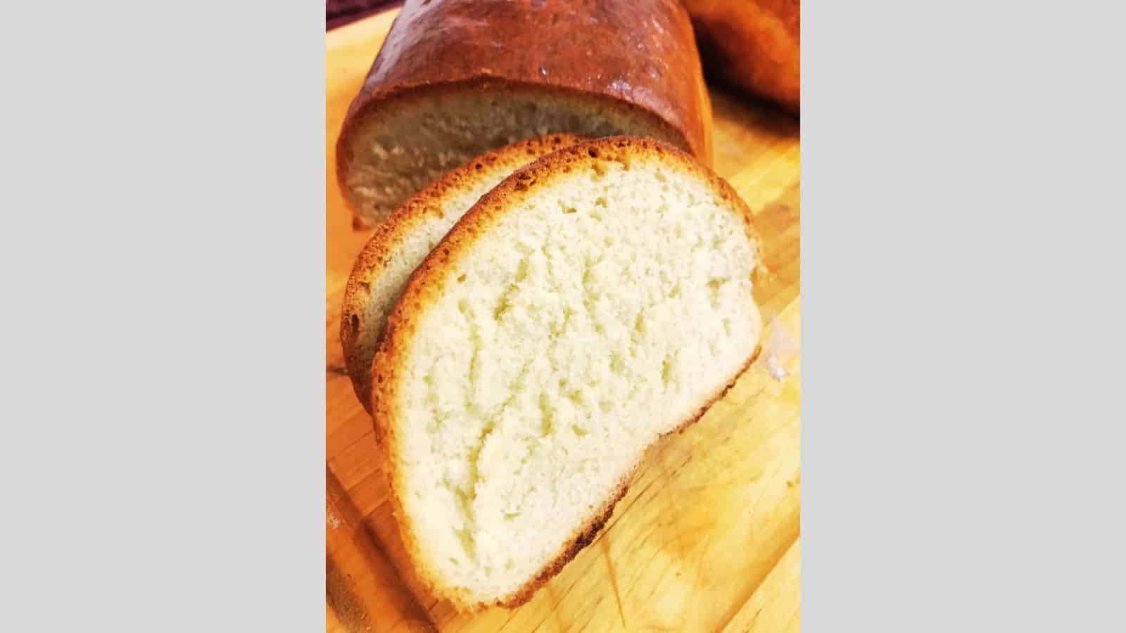 A sliced loaf of white bread rests on a wooden surface, revealing its light, fluffy interior and golden crust.