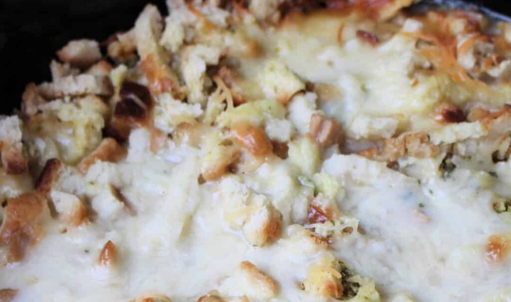 A crock pot filled with casserole topped with stuffing and cheese.