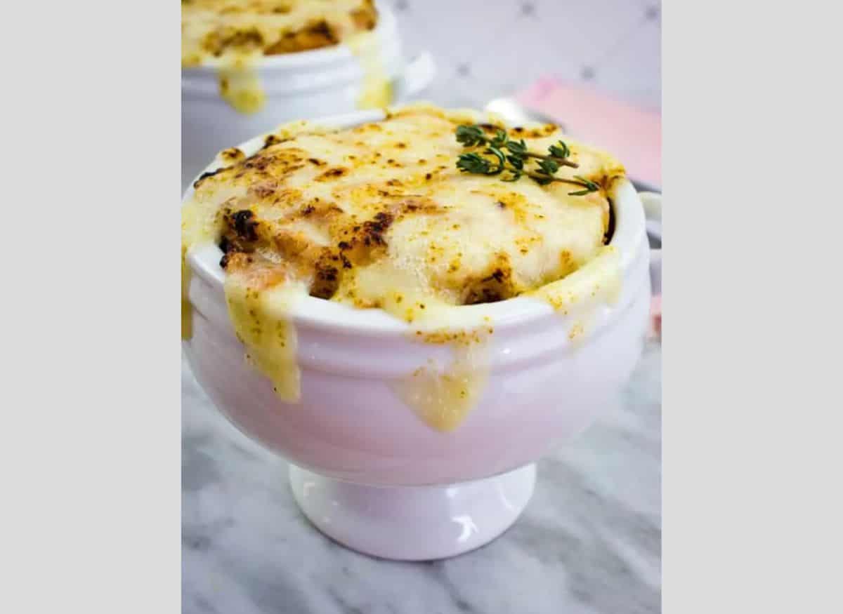 Low-Carb French Onion Soup in a tall white bowl on a marble counter.