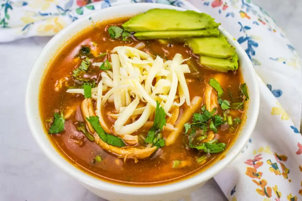 Low-Carb Chicken Tortilla Soup in a white bowl next to a floral cloth.