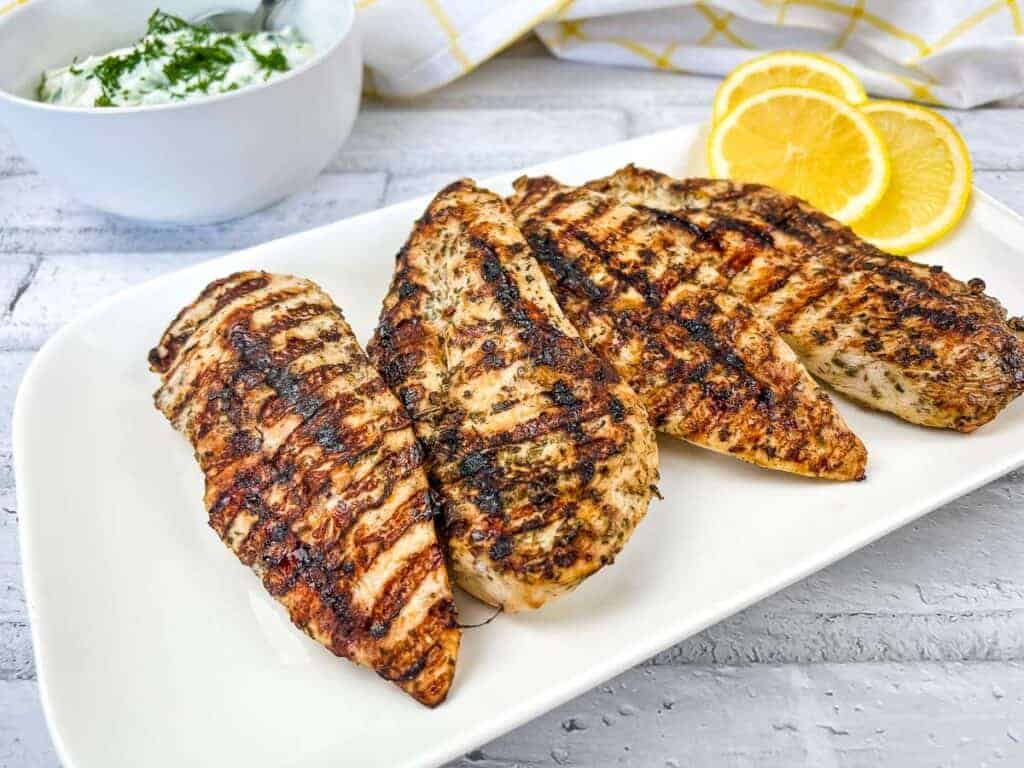 Grilled Greek Chicken on a white plate with lemon slices.