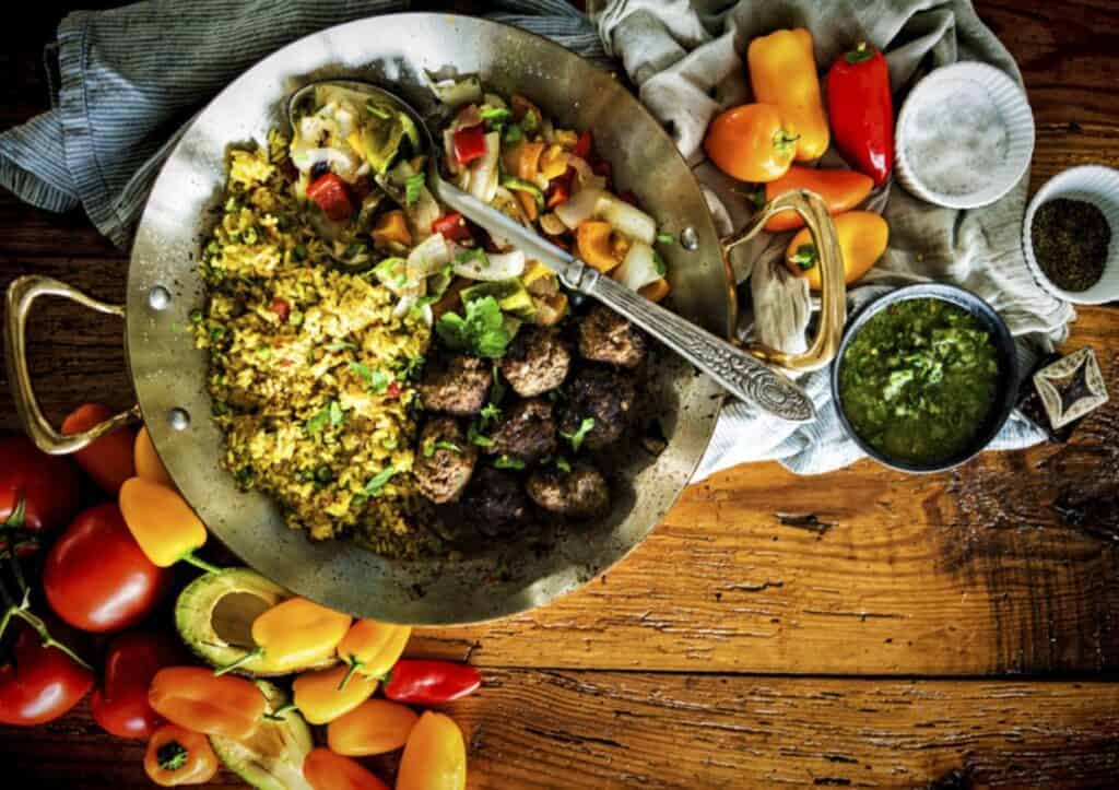 Bit metal platter of rice, veggies and meatballs.