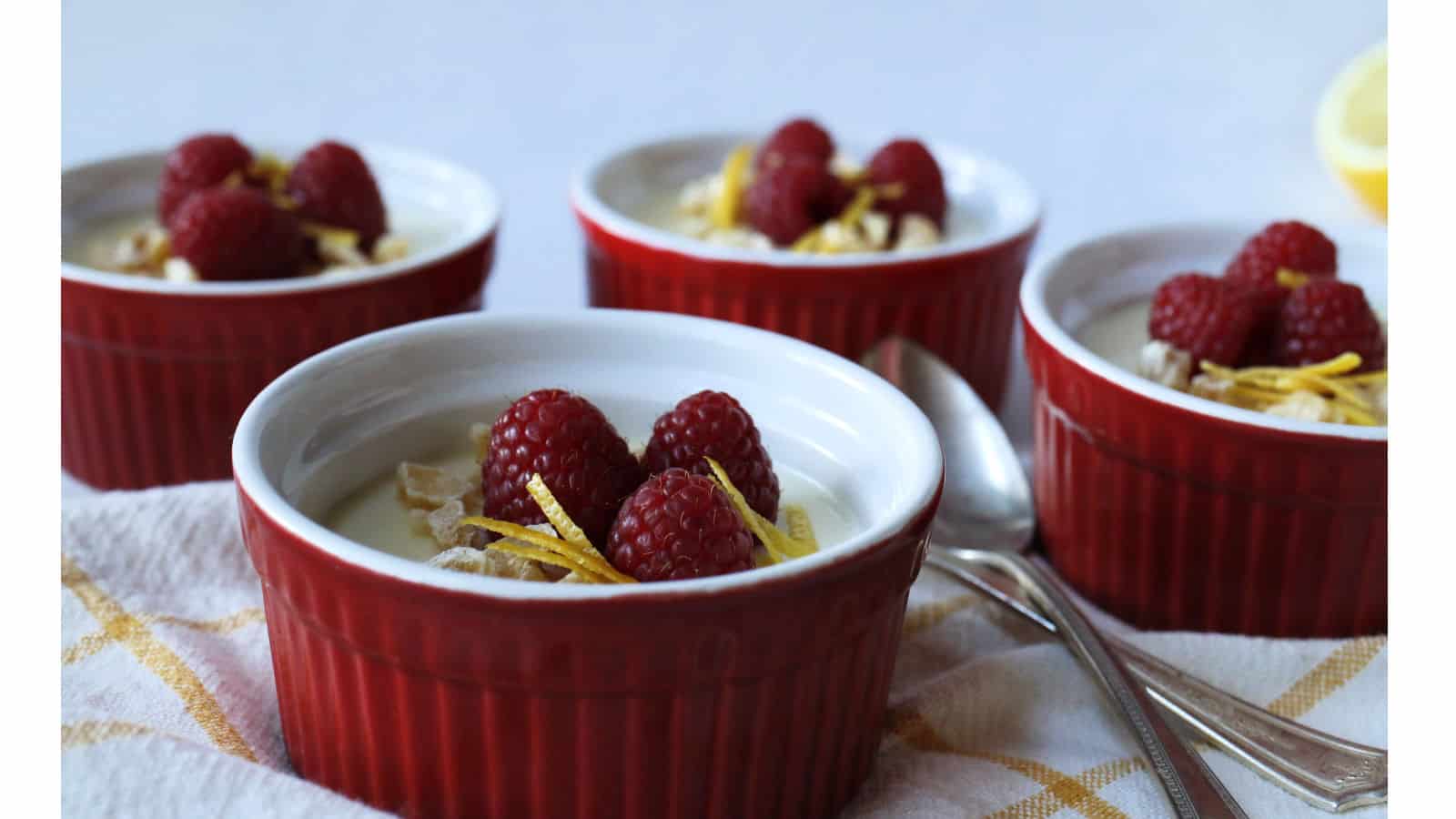 Lemon posset in red ramekins on a yellow and white towel.